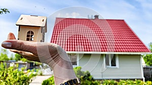 Small wooden toy house on palm of woman hand and big home on background. symbol and concept of cconstruction, buying