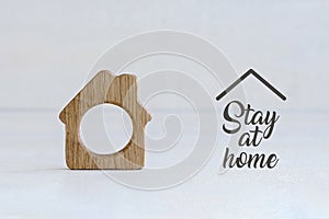 Small wooden toy house on white pastel background with words stay at home