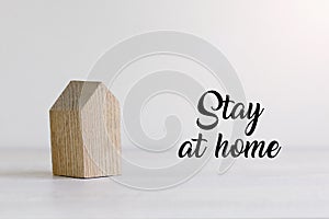 Small wooden toy house on white pastel background with words stay at home