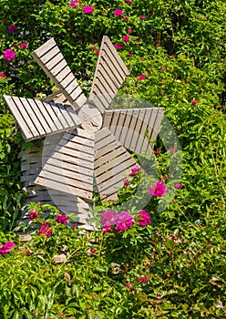 A small wooden windmill in the beautiful summer garden. Windmill and roses. Garden furniture