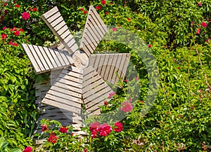 A small wooden windmill in the beautiful summer garden. Windmill and roses. Garden furniture