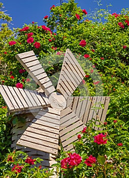 A small wooden windmill in the beautiful summer garden. Windmill and roses. Garden furniture