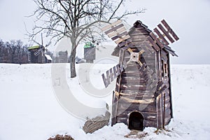 Small wooden windmill in foreground with focus on it and big historical windmills in background against background of winter lands