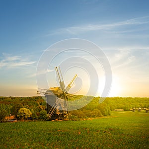 small wooden windmill among green rural fields at the sunset