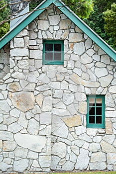 Small wooden windows and chimney stack in a stone cottage with green trim and gable