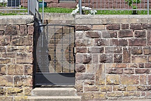 A small wrought iron door in front of the house and a stone fence.