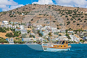 Small yacht with tourists, hotels and tourist resort, in Mirabello Bay, Crete island, Greece