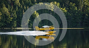 Small yellow airplane on pontoons takes off from a lake.