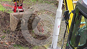 A small yellow excavator works near the building â€“ excavator loading soil and roots.