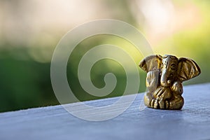 Small yellow Ganesha figure with unfocused background. Beautiful golden Ganesh statue with open palm. Asian religion concept.