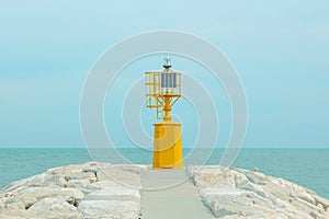 Small yellow lighthouse at the end of the pier against the blue sea and pastel sky