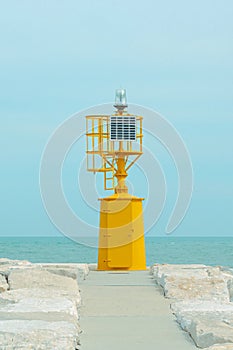 Small yellow lighthouse at the end of the pier against the blue sea and pastel sky