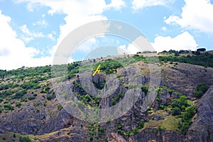 Small yellow propeller airplane maneuvering close to the ground with rocky hill at the background