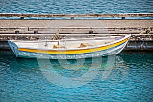 Small yellow rowboat tied to the dock with reflections in the water