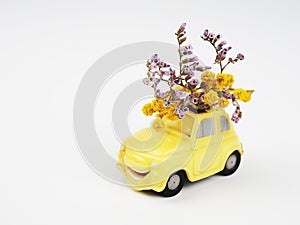 Small yellow toy car with a bouquet of wild flowers on a white background