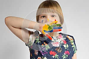 A small young girl covers her face with a paint-stained hand