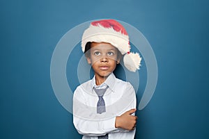 Smart african american kid boy student in Santa hat looking up on blue background. Little black child school boy