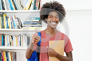 Smart african american male student with backpack and paperwork showing thumb up