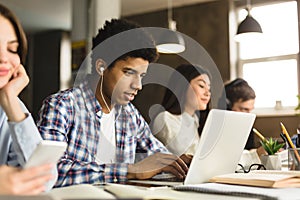 Smart afro guy studying in university library, using laptop