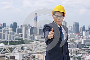 Smart Asian businessman engineer wear yellow safety helmet hardhat showing thumb up for successful job standing roof top building