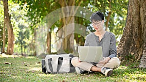 Smart Asian male college student using his laptop, doing his school project in the campus park