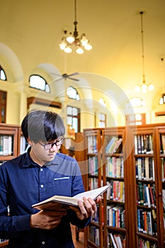 Smart Asian man student reading book in library