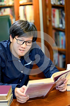 Smart Asian man student reading book in library