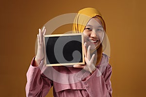 Smart Asian Muslim Teenage Girl Smiling at Camera and Showing Empty Blackboard