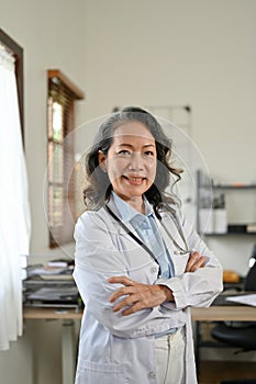 Smart Asian senior female doctor arms crossed, stands in the doctor`s office