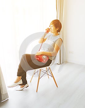 Smart Asian woman sitting and holding red vintage phone