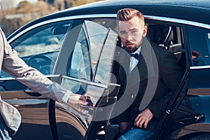 Smart attractive businessman is going out from car while his assistant is opening door for him.