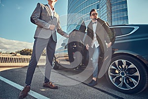 Smart attractive businessman is going out from car while his assistant is opening door for him.