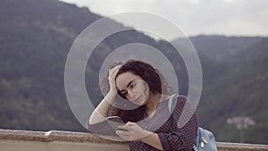 Smart, beautiful brunette corrects curly hair and prints sms on the phone at against the backdrop of outstanding