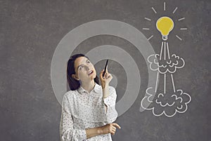 Woman with pen looking at flying light bulb rocket and thinking of her own business startup idea