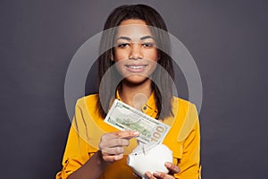 Smart black woman putting in piggy bank one hundred dollars banknote