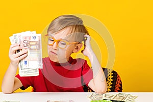 Smart boy counting money at table over yellow background. Future savings