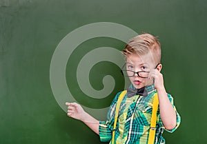 Smart boy points on empty green chalkboard