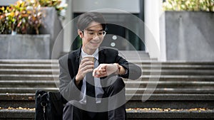 A smart businessman is sipping coffee and checking time on his watch while sitting on a staircase