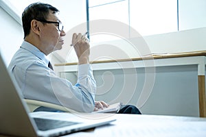 Smart businessman sitting serious thinking on a chair in the office  his hand hold the pen with more copy space