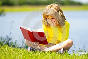 Smart child boy reading book in park outdoor. Blonde kid reading a book in summer. Clever kids outdoor portrait. Kids