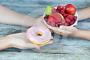 Smart child choosing healthy fruits in white bowl instead of coloury but unhealthy donut
