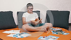 Smart Child in Glasses Reading an Interesting Book Sitting on Floor in the Room