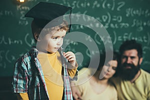 Smart child in graduate cap like to perform. Boy presenting his knowledge to mom and dad. Parents listening their son