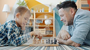 Smart child playing chess with dad at home lying on floor together having fun