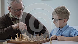 Smart child playing chess with grandfather, family having fun, early development