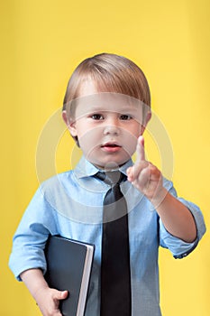 Smart child, portrait of a boy with a book in his hands on a yellow background shows up his index finger, genius kid