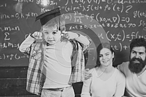 Smart child. Wunderkind concept. Smart child, wunderkind in graduate cap pointing at his head. Parents listening their