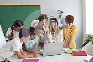 Smart children pupil boys and girls stand in front of laptop with woman teacher in primary school