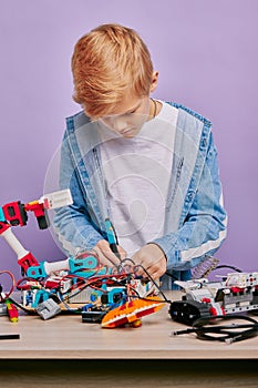 Smart clever kid boy in casual wear assemble robots
