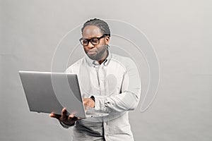 Smart African-American man using a laptop, isolated on grey